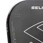 Close-up van de Selkirk LABS 007 Invikta pickleball paddle, zwart blad met rode onderzijde, wit handvat en het Selkirk-logo in zwart met witte omlijning op het slagooppervlak.