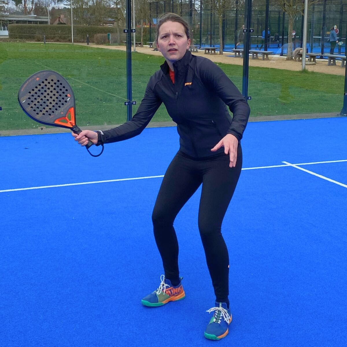 Padel speelster op veld met zwarte leggings en zwart vestje van Pace